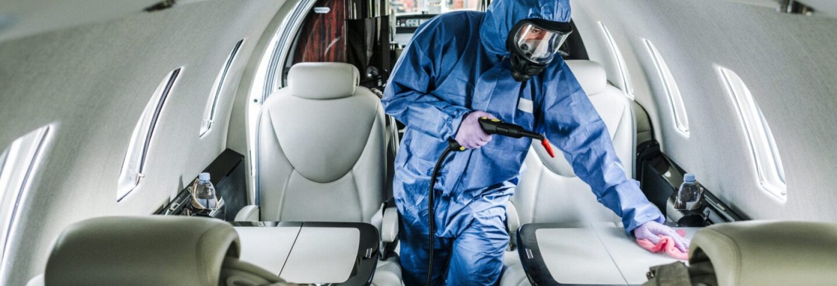 A cleaner in blue coveralls disinfecting the passenger cabin before the passengers arrival